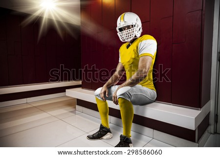 Football Player with a yellow uniform seated in locker room.