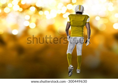 Football Player with a yellow uniform walking, showing his back on a yellow lights background.