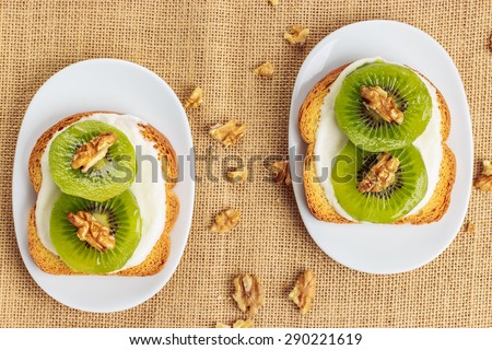 Toast with kiwi, cheese and walnuts on a piece of sackcloth with walnuts around. View from above