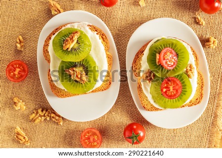 Toast with kiwi, cheese, walnuts and cherry tomato  on a piece of sackcloth with walnuts and cherry tomatoes around. View from above