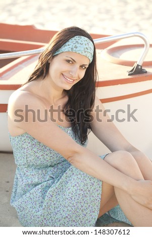 Beautiful young woman sitting by a boat at the beach