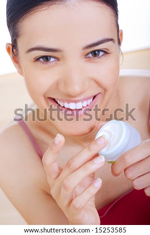 young smiling woman applying cream on her face