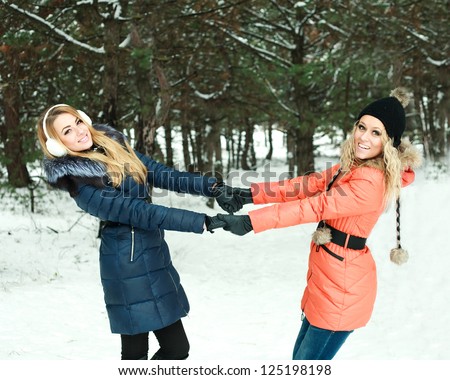 Portrait of two happy girls holding hands, in pinewood, on a winter day