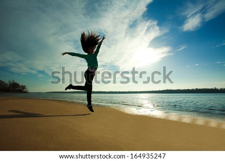 Woman jumping on the beach on sunny sky background, freedom and health concept