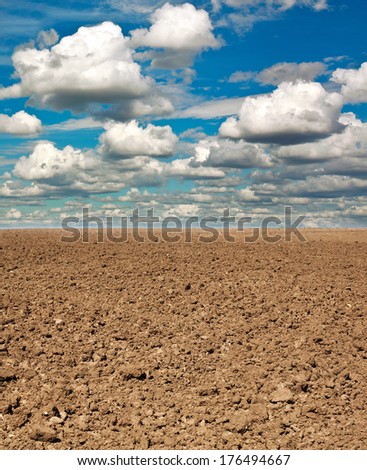 Dry plowed earth agricultural land, on background blue sky and white clouds