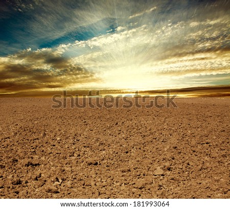 Plowed farmland field on the background of cloudy sky in sunset rays