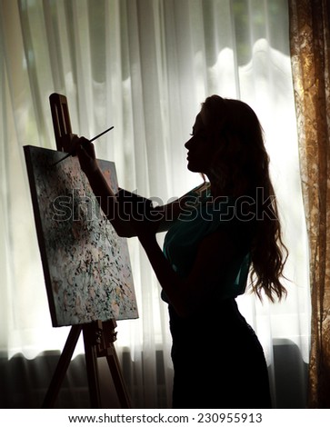 Silhouette woman artist draws paint picture on easel, portrait indoor