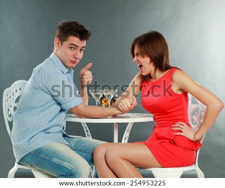 Young aggressive woman winning fighting in arm-wrestling at table, in studio isolated on gray
