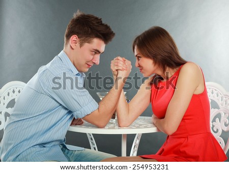 Young happy couple challenge fighting in arm-wrestling at table, in studio isolated on gray