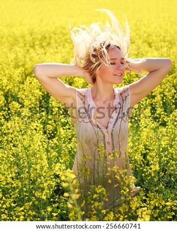 Happy carefree summer girl in rape field. Cheerful young woman joyful in spring, smiling with arms raised up, and closed eyes
