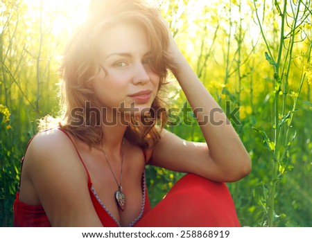 Young woman sitting in green grass in sunlight, dreaming in summer time