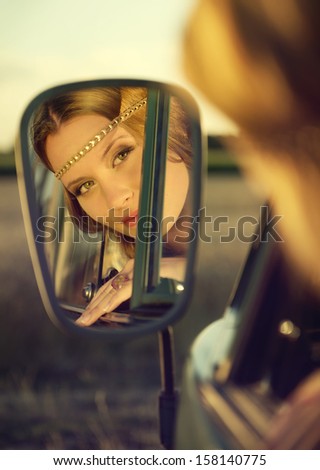 face of an attractive brunette woman in the rear mirror of an old car