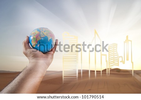 Hand holding a Globe. Buildings of Development on a Desert Landscape