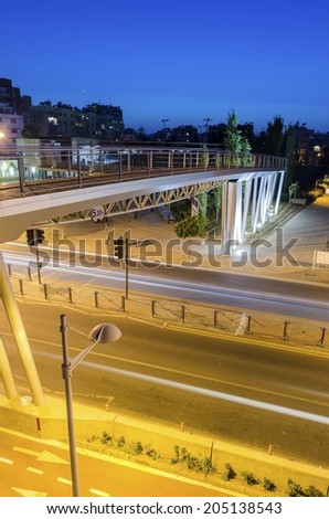 A night view of the seaside bridge connecting the beach to GSO Sports park in Limassol, Cyprus. A view of the street, the wooden and glass pedestrian bridge, Fytideio sports park and paraliakos.