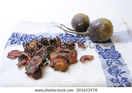 Thin round beetroot chips baked in the oven with oregano and salt and ripe beet roots in the white background. A healthy, vegetarian, vegan, crispy snack appetiser for diet and clean eating.