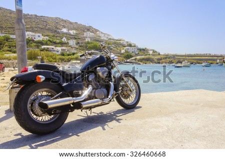 An old vintage motorbike parked at Ornos beach in Mykonos, Greece. A concept of freedom, summer and holiday vacations on the beautiful greek island and the crystal clear blue sea.