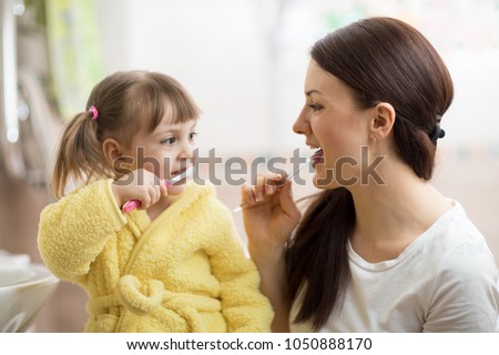 mom teaching daughter child teeth brushing in bathroom