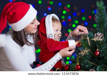child girl with mother decorating Christmas tree on bright background