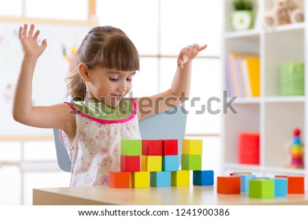 Little girl build block toys at home or daycare. Cheerful kid playing with color cubes. Educational toys for preschool and kindergarten children.