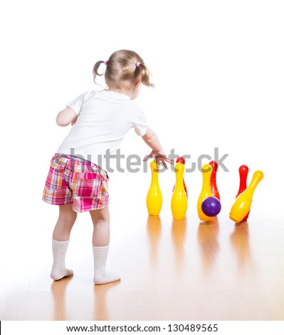 Kid throwing ball to knock down toy bowling pins. Focus on child girl standing back.