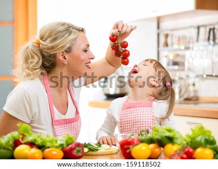 mother preparing dinner and feeding kid tomatoes in kitchen