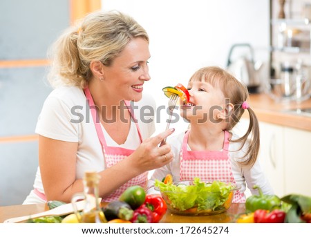 mother feeding kid daughter vegetables in kitchen