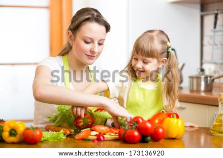 mother teaching kid daughter preparing salad at kitchen