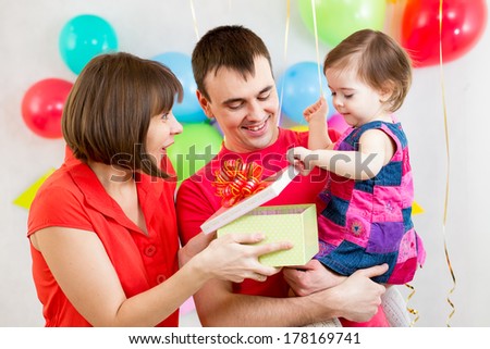 smiling kid girl with mother and father opening gift box