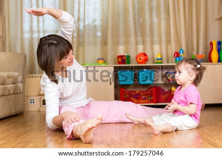 Mom and kid doing exercises sitting on the floor in home interior