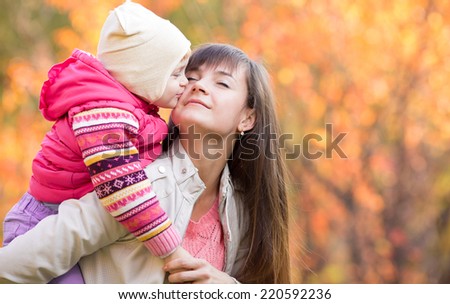 Beautiful woman with kid girl outdoors in fall. Child kissing mom. Mothers day holiday concept.