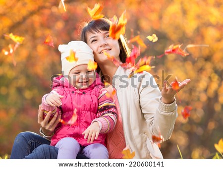 Kid and beautiful mother play and throw leaves outdoor in autumn park