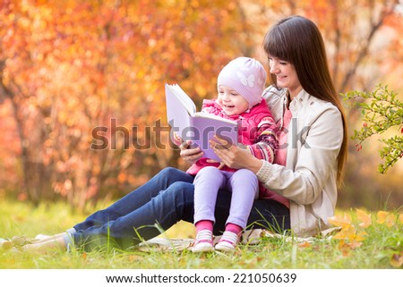 mother reading a book to kid outdoors in fall