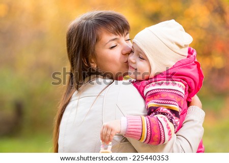 Happy woman and kid in golden autumn background. Mom kissing daughter. Mothers day holiday concept