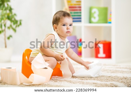 kid boy sitting on chamber pot with toilet paper roll