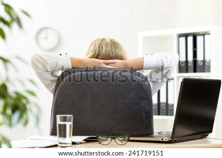 Businesswoman relaxing in office sitting back in chair with hands behind neck