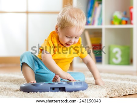 Happy kid toddler boy having fun playing piano toy in nursery