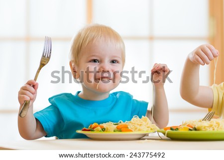 kid eating spaghetti with vegetables in nursery or at home