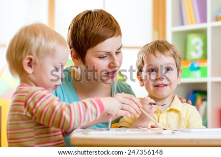 cute woman teaching kids to paint at nursery or playschool