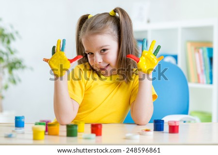 kid girl showing painted hands sitting at table in nursery