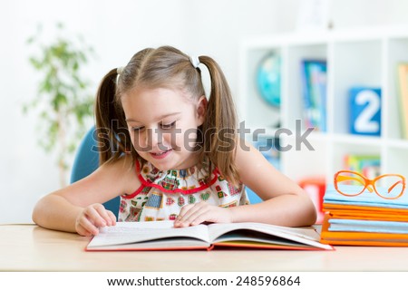 Child girl learns to read sitting at table in nursery