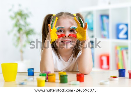 cute cheerful kid girl showing her hands painted in bright colors