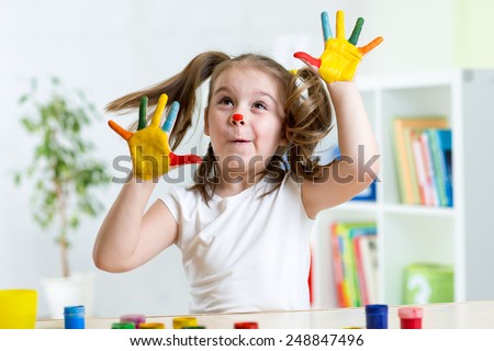 Child girl having fun, her face and palms covered with paint