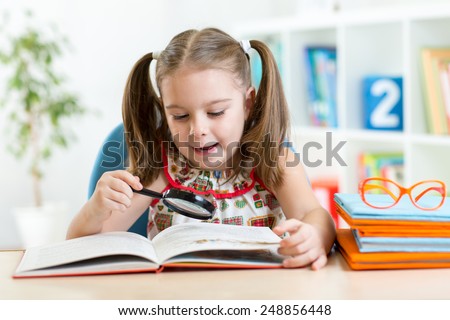 Astonished kid looking through a magnifying glass with book at home