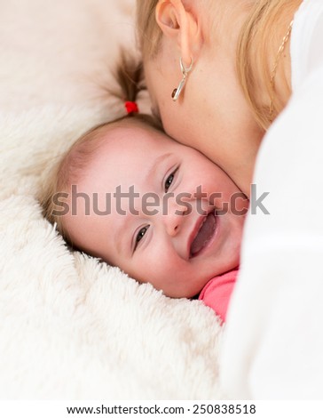 Happy mother kissing baby daughter lying on bed