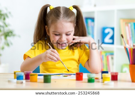 smiling kid girl painting with paintbrush at home or day care center
