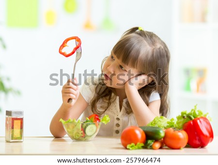 Cute kid girl not wanting to eat healthy food at kitchen