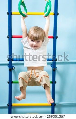 cute child boy hanging on gymnastic rings at home