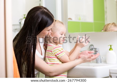 mom teaches child hands washing with soap in bathroom