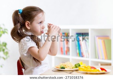 Cute kid girl drinking water sitting at table in home