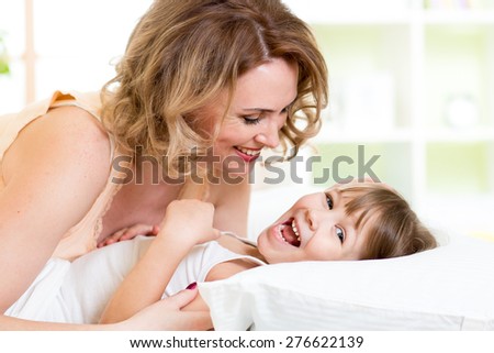 happy family - kid with mother play, laugh and tickle in white bed in bedroom